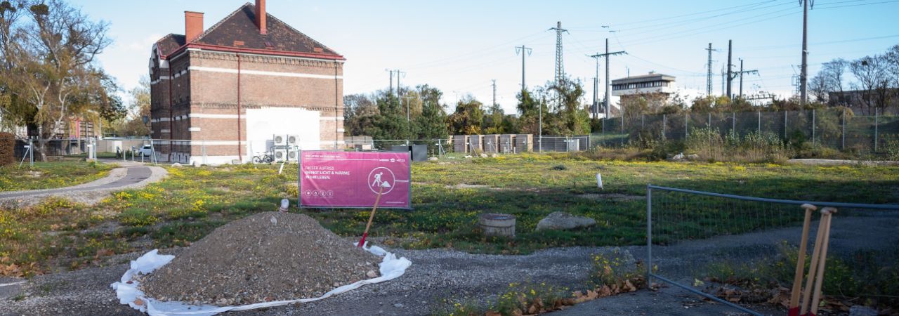 Erdhaufen mit Spaten vor einer grünen Wiese im Hintergrund ein Backsteinhaus.