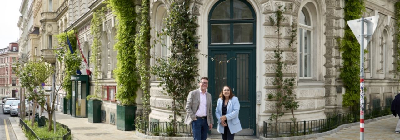 Futónövényekkel körbeültetett történelmi épület előtt két ember